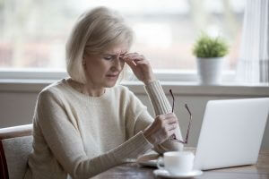 Older woman rubbing her eyes in front of lap top