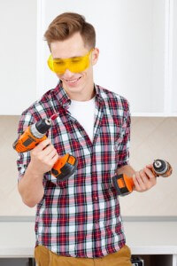 Young man in plaid shirt with power tools and safety glasses