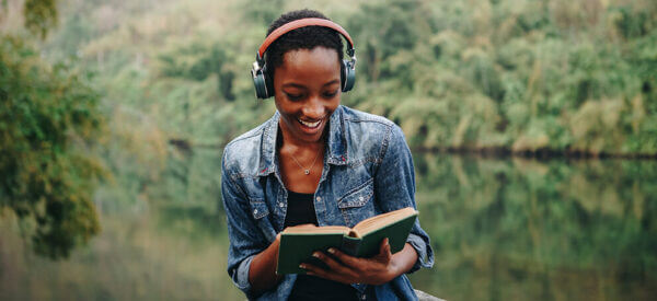 Woman reading with headphones next to lake