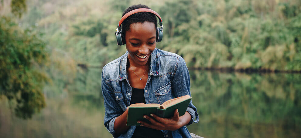 Woman reading with headphones next to lake